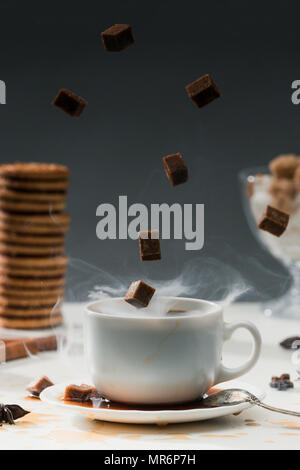 Steaming coffee cup with falling cane sugar cubes by cookies on table Stock Photo