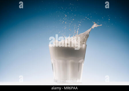 Glass with milk and splashes isolated on blue background Stock Photo