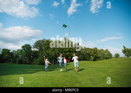 Cheerful multiethnic kids playing together while running with kite in park Stock Photo