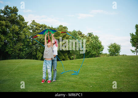 Adorable happy children playing with kite on green grass in park Stock Photo