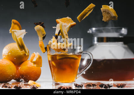 Glass cup of hot steaming tea with falling citrus pieces Stock Photo