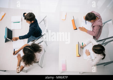 Overhead view of pupils using digital tablets while sitting at desks in classroom Stock Photo