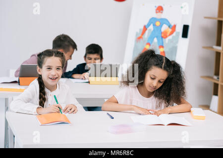 Multiethnic group of pupils writing in exercise books and using digital tablets during lesson Stock Photo