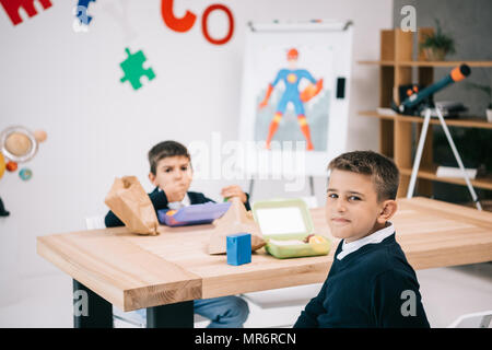 Two caucasian schoolboys eating lunch while sitting at wooden table Stock Photo