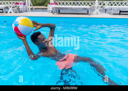 Young happy african american man playing with ball in swimming pool Stock Photo