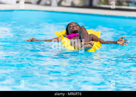 African american woman floating on inflatable mattress in swimming pool Stock Photo