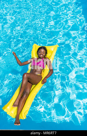 African american woman floating on inflatable mattress in swimming pool Stock Photo