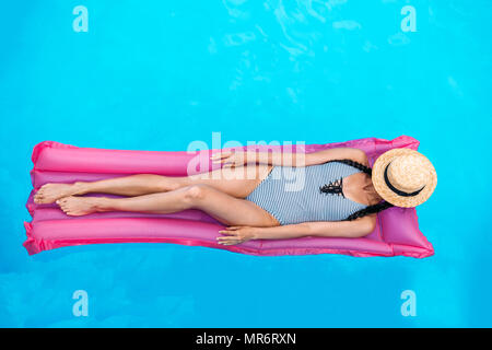 Young woman with straw hat covering face floating on air mattress in swimming pool Stock Photo