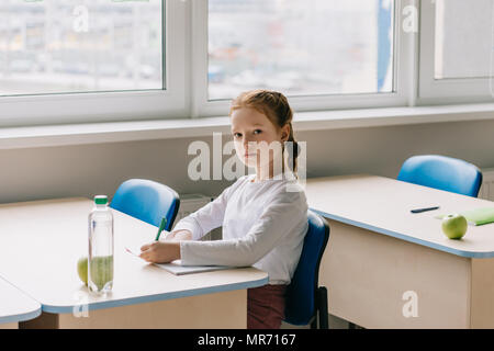 beautiful little schoolgirl writing in classroom at school Stock Photo