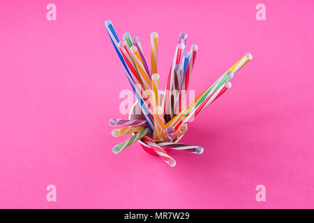 a bundle of multi-colored drinking straws in a paper Cup on a pink background. fashion minimal. flat lay Stock Photo
