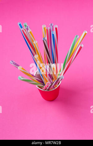 a bundle of multi-colored drinking straws in a paper Cup on a pink background. fashion minimal. flat lay Stock Photo