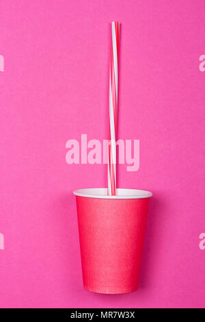 a bundle of multi-colored drinking straws in a paper Cup on a pink background. fashion minimal. flat lay Stock Photo