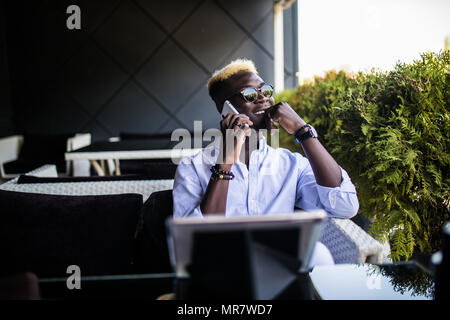 Afro man talks on the phone in a nice cafe. Smile in the conversation. Stock Photo