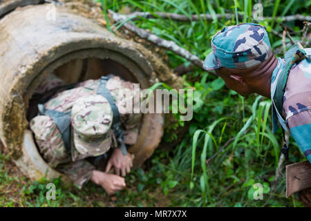 Ghanaian Armed Forces Sgt. Ibrahim Abubakari observes a U.S. Soldier from 1st Battalion, 506th Infantry Regiment, 1st Brigade Combat Team, 101st Airbone Division crawl through an obstacle during United Accord 2017 at the Jungle Warfare School in Achiase military base, Akim Oda, Ghana, May 20, 2017. The Jungle Warfare School is a series of situational training exercises designed to train participants in counter-insurgency and internal security operations. (U.S. Army photo by Spc. Victor Perez Vargas) Stock Photo