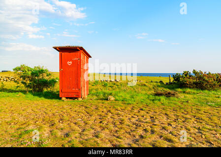 Lovely little red outhouse on a coastal meadow on a sunny day. Stock Photo