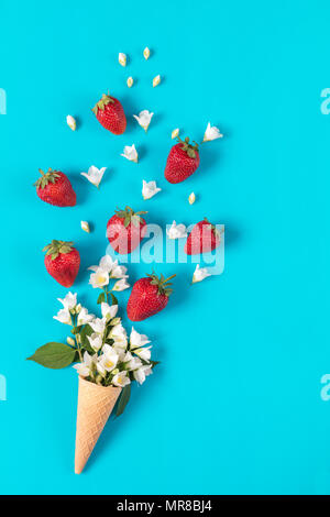 Cup of tea with fresh strawberries and flowers jasmine blossom bouquets on blue surface. Flat lay, top view sweet food floral background. Stock Photo