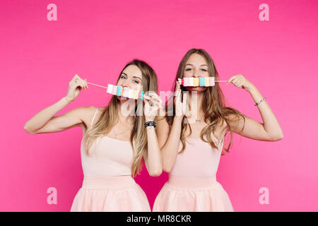 Beautiful girls like dolls having fun with marshmallow candies on stick. Stock Photo