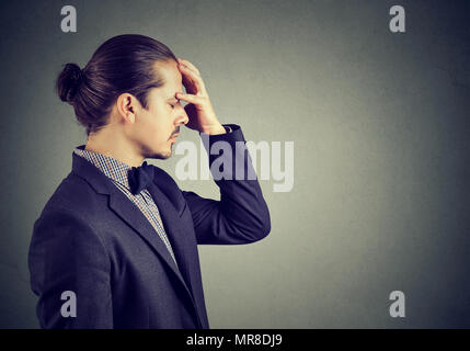 Profile of young handsome man in suit holding hand on forehead concentrating on idea and looking worried. Stock Photo