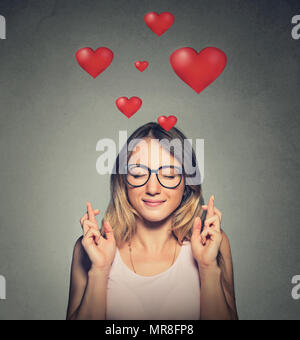 Portrait of a hopeful beautiful woman in love crossing her fingers, eyes closed, hoping for the best isolated on wall background. Stock Photo