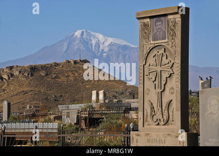 Mount Ararat looms behind a cemetery next to Khor Virap Monastery in Armenia. Many tombstones include photographs of the deceased. Stock Photo