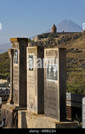 The peak of Little Mount Ararat rises behind a cemetery below Khor Virap Monastery in Armenia. Many tombstones include photographs of the deceased. Stock Photo