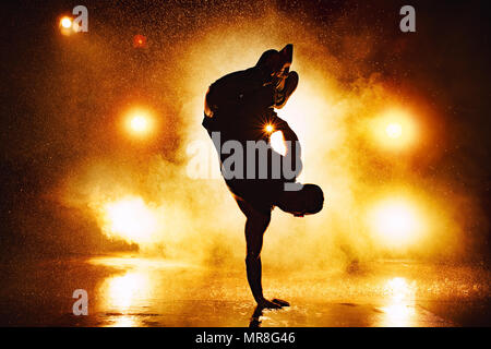 Young man break dancer dramatic silhouette standing on hand in club with lights and water. Tattoo on body. Stock Photo