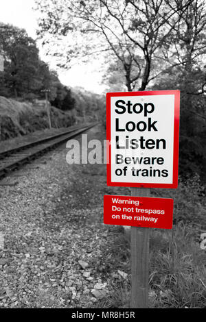 Railway warning sign in black and white with red signpost reading 'Stop Look Listen Beware of trains' with a railway running off into the distance. Stock Photo