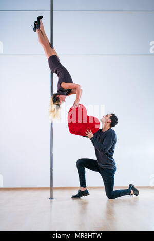 Young man and woman pole dancers. Man expressing feelings and giving big red heart. Love concept. Stock Photo
