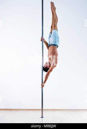 Young pole dancing man on white wall background Stock Photo