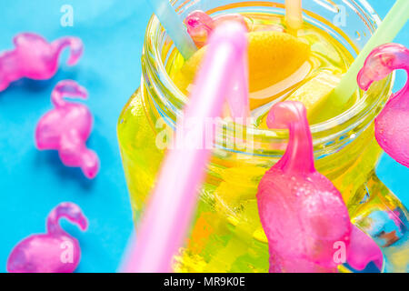 Ice cold Lemonade in glass jar with straws and icy plastic flamingos isolated on blue backdrop Stock Photo