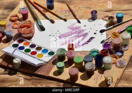 Background image showing interest in watercolor painting and art. A painted sheet of paper, surrounded by brushes, jars of watercolor paint and gouach Stock Photo