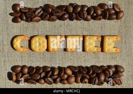 Background of a gray canvas made of old and coarse burlap, on which lies a certain amount of brown coffee beans and the word "coffee", composed of edi Stock Photo