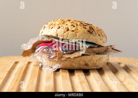 Fresh tasty burger with plastic waste and paper cardboard inside on wooden board. Recycled waste in our food concept. Stock Photo