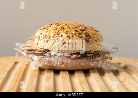 Fresh tasty burger with plastic waste and paper cardboard inside on wooden board. Recycled waste in our food concept. Stock Photo