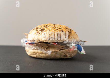 Fresh tasty burger with plastic waste and paper cardboard inside on dark background. Recycled waste in our food concept. Stock Photo