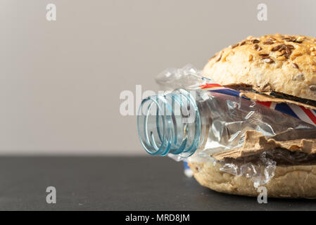 Fresh tasty burger with plastic waste and paper cardboard inside on dark background. Recycled waste in our food concept. Stock Photo