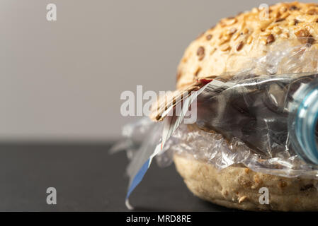 Fresh tasty burger with plastic waste and paper cardboard inside on dark background. Recycled waste in our food concept. Stock Photo