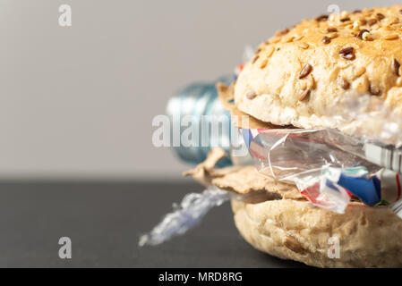 Fresh tasty burger with plastic waste and paper cardboard inside on dark background. Recycled waste in our food concept. Stock Photo