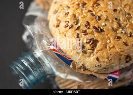 Fresh tasty burger with plastic waste and paper cardboard inside on dark background. Recycled waste in our food concept. Stock Photo