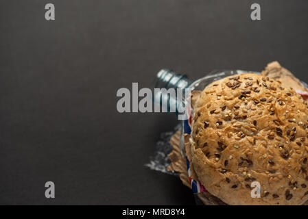 Fresh tasty burger with plastic waste and paper cardboard inside on dark background. Recycled waste in our food concept. Stock Photo