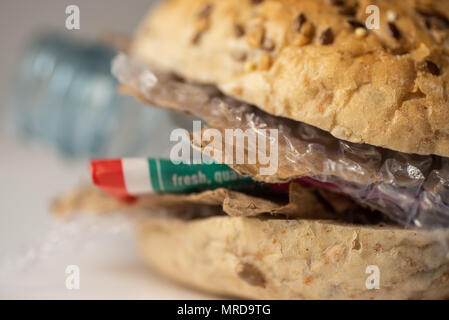 Fresh tasty burger with plastic waste and paper cardboard inside on white background. Recycled waste in our food concept. Stock Photo