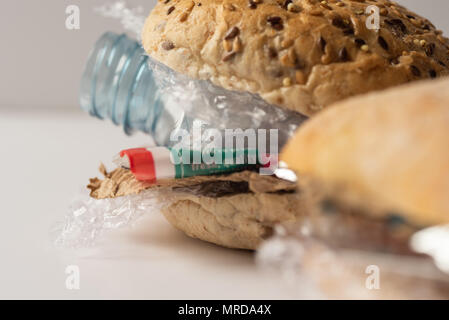 Fresh tasty burger with plastic waste and paper cardboard inside on white background. Recycled waste in our food concept. Stock Photo