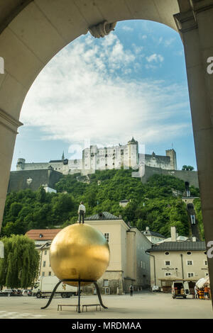 Kapitelplatz square, Salzburg, Austria. Sphaera sculpture (Man on Golden Mozart ball) foreground & medieval fortress of Hohensalzburg behind. Stock Photo