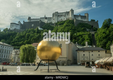 Kapitelplatz square, Salzburg, Austria. Sphaera sculpture (Man on Golden Mozart ball) foreground & medieval fortress of Hohensalzburg behind. Stock Photo