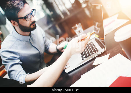 Young bearded businessman in glasses analyzes the teamwork done. Works at the desk with a laptop and office accessories. Blurred background Stock Photo