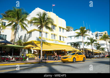 MIAMI - JANUARY 12, 2018: Restaurants on the tourist strip of Ocean Drive stand ready for morning customers in South Beaches a taxi drives past.