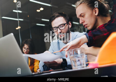 Young team of coworkers making new project on modern big loft office. People working planning start up. Contemporary notebook on wood table Stock Photo
