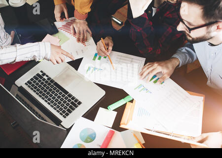 Young coworkers discussing  charts and graphs showing the results of their successful teamwork.  Laptop and paperwork on the table Stock Photo