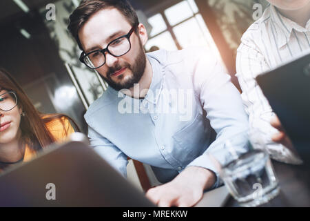 Group of coworkers sitting at a wooden table and working on laptops in a modern loft office. Young entrepreneurs are working on a new project Stock Photo