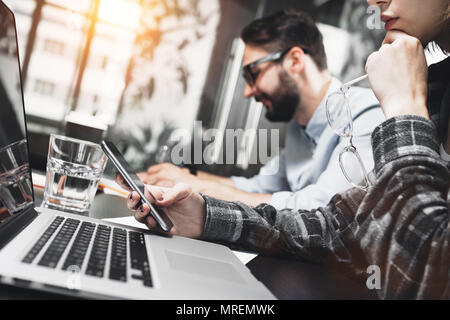 Woman manager thinks over the project and keeps the glasses in hand in the loft studio. Team of young project managers working with modern laptop and  Stock Photo